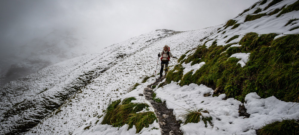 Caminhante atravessando trecho nevado da Via Alpina