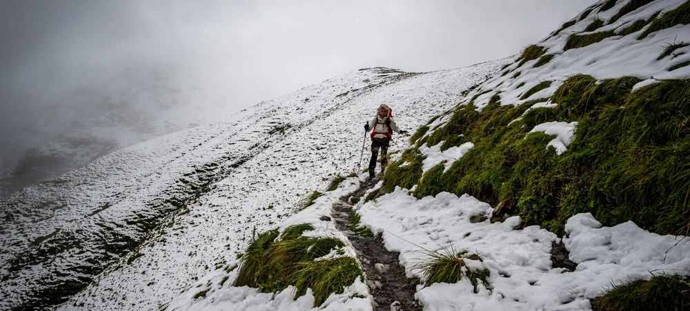 Caminhante atravessando trecho nevado da Via Alpina
