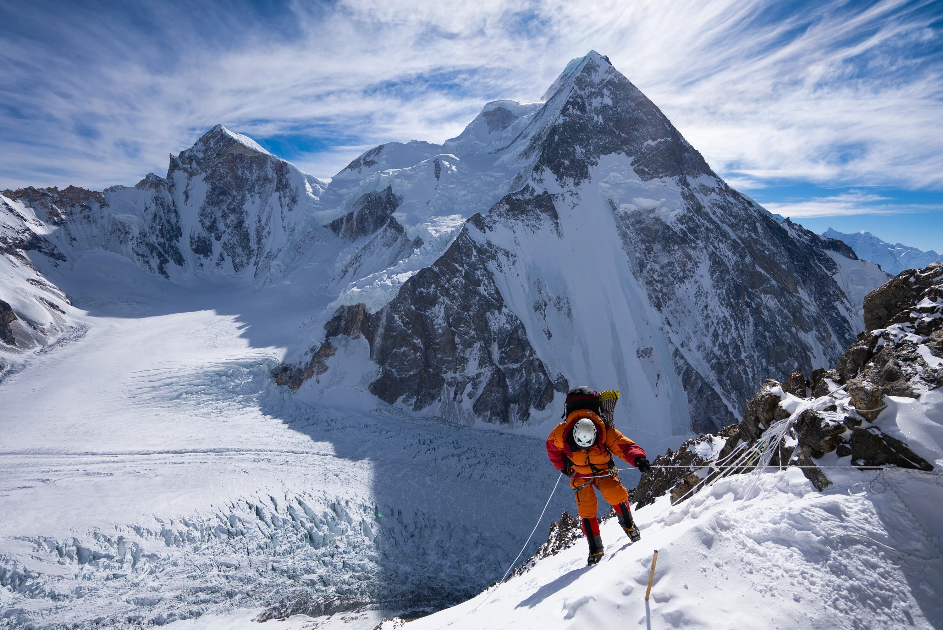 Alpinista sobe uma encosta nevada diante de grandes montanhas
