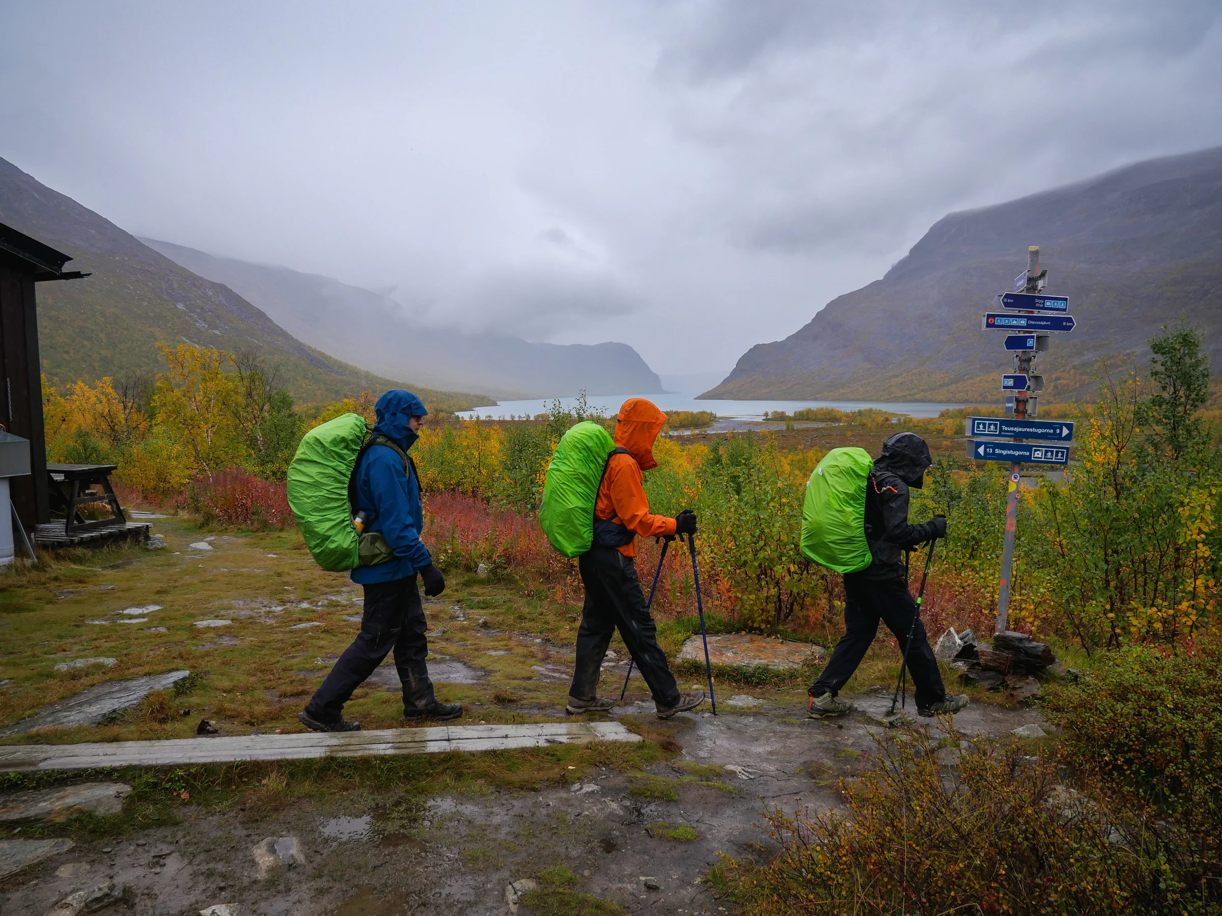 Caminhantes passam por placas de orientação em um dia de chuva na Kungsleden.
