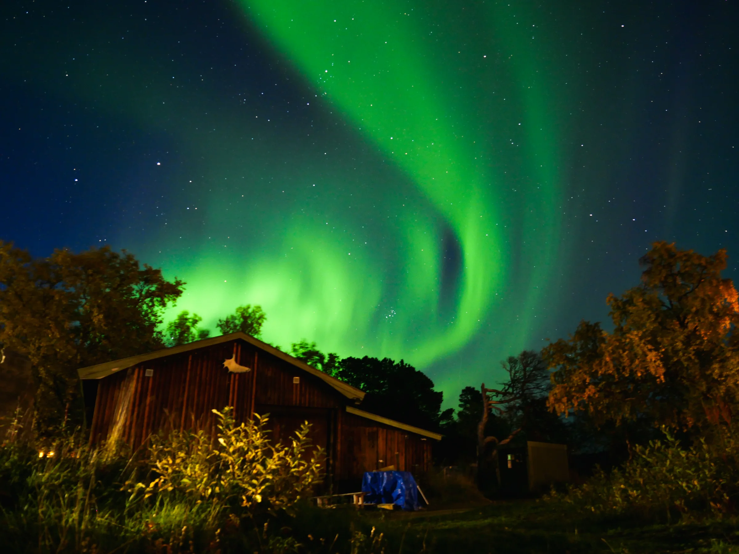 Aurora boreal ilumina o céu sobre uma cabana durante a viagem pela Suécia.