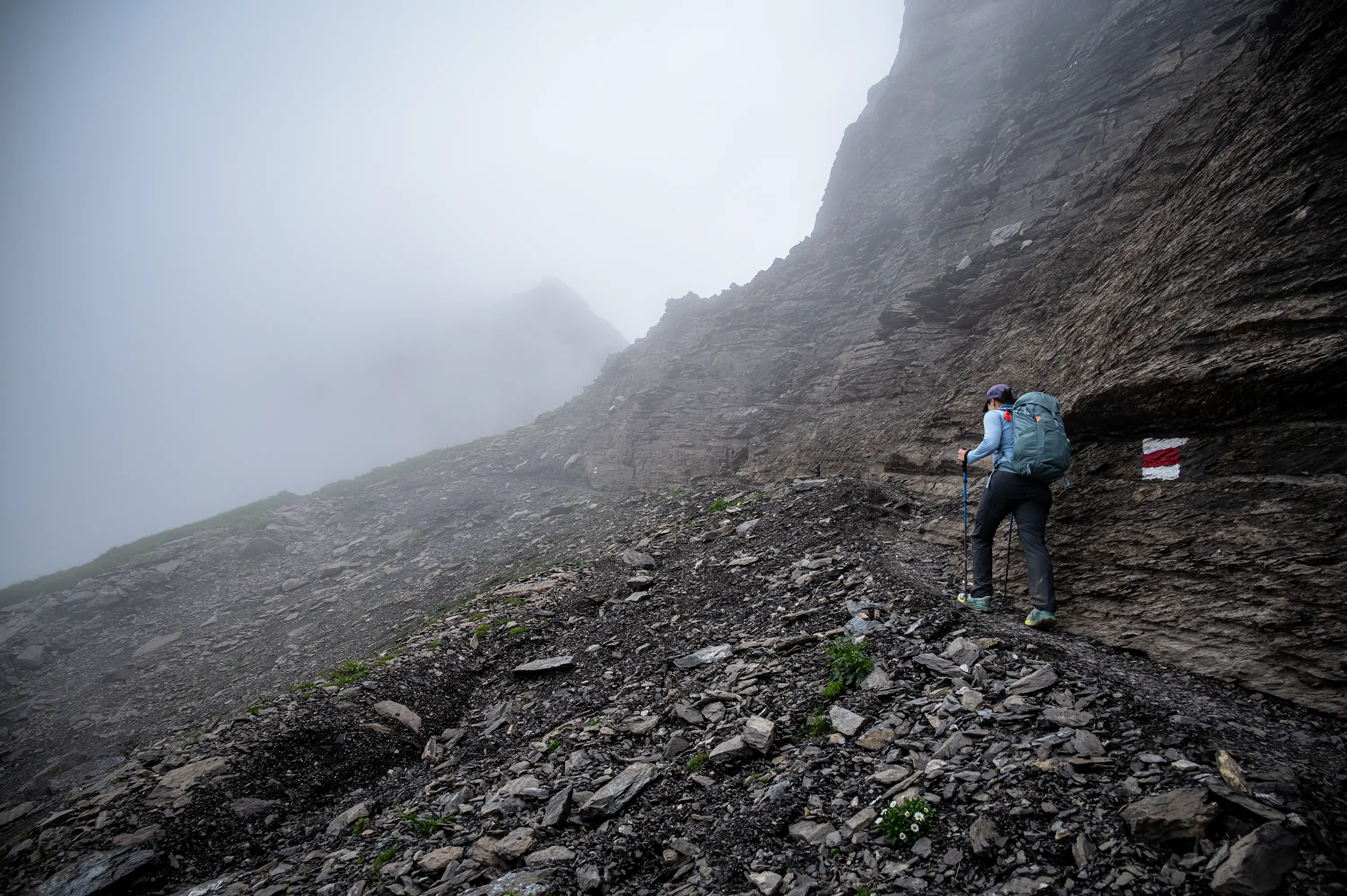 Um caminhante segue por um trecho rochoso dos Alpes, sob neblina.