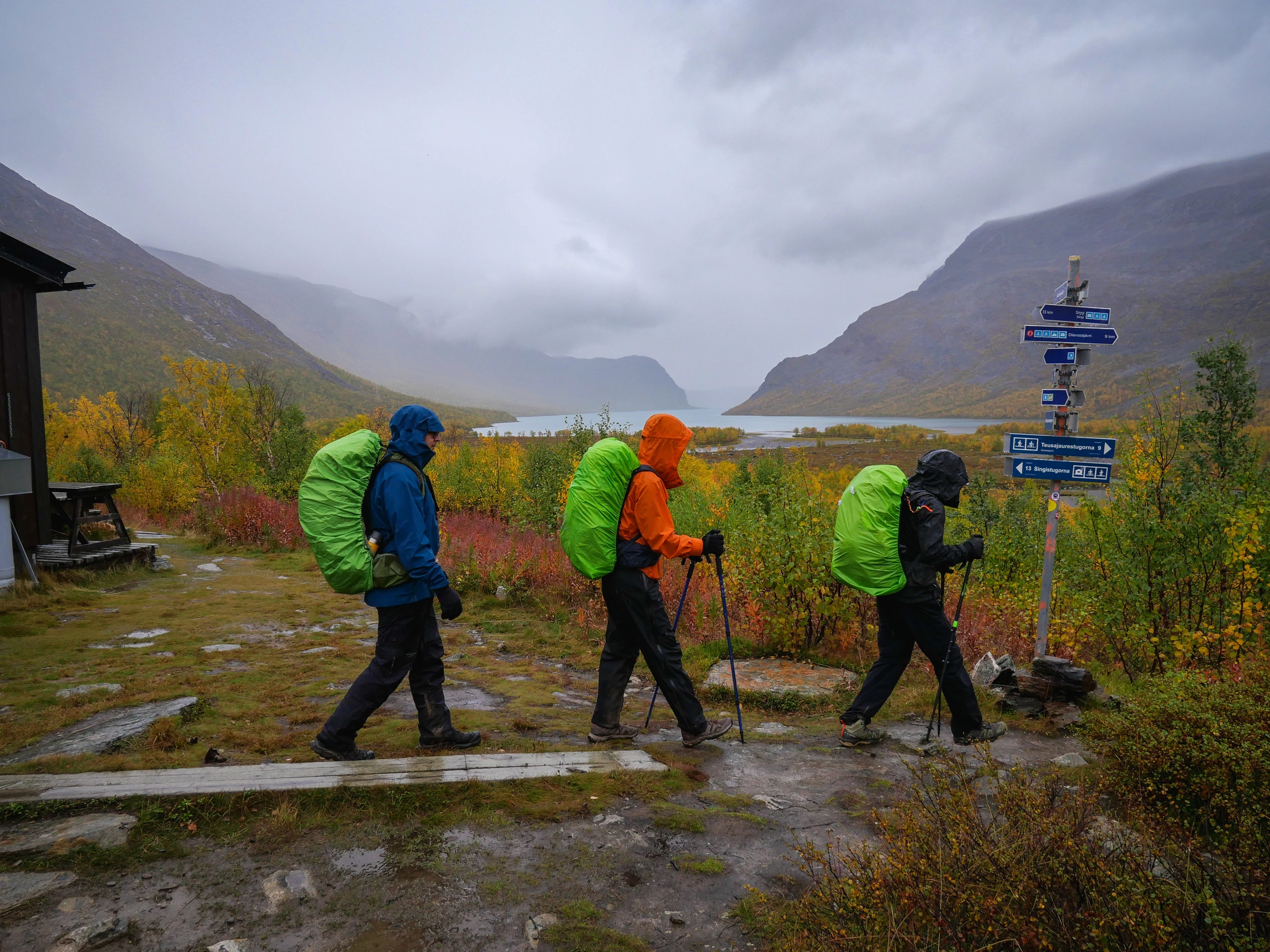 Caminhantes passam por placas azuis em um dia de chuva na Kungsleden.